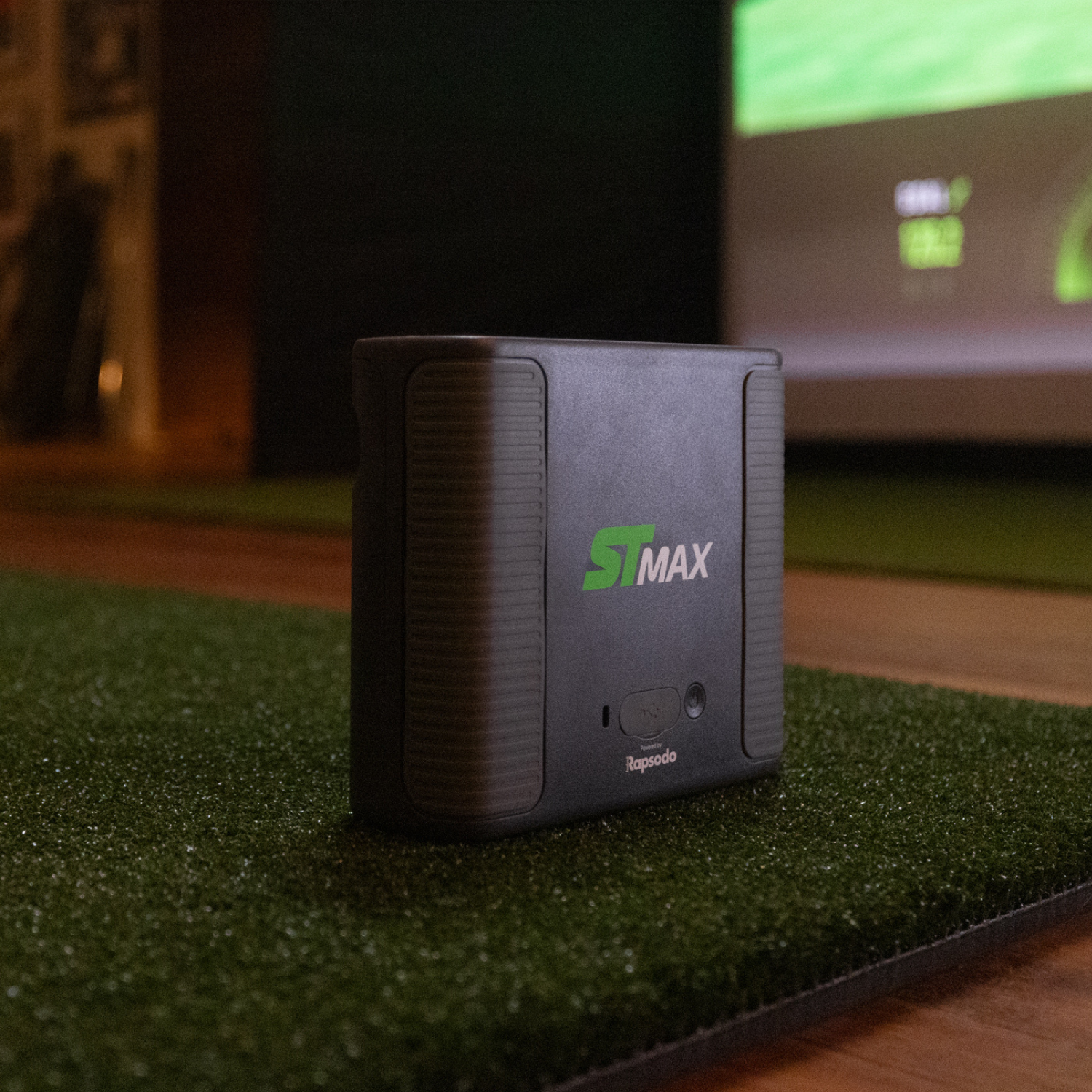Black ST Max launch monitor device on a green surface with a blurred background