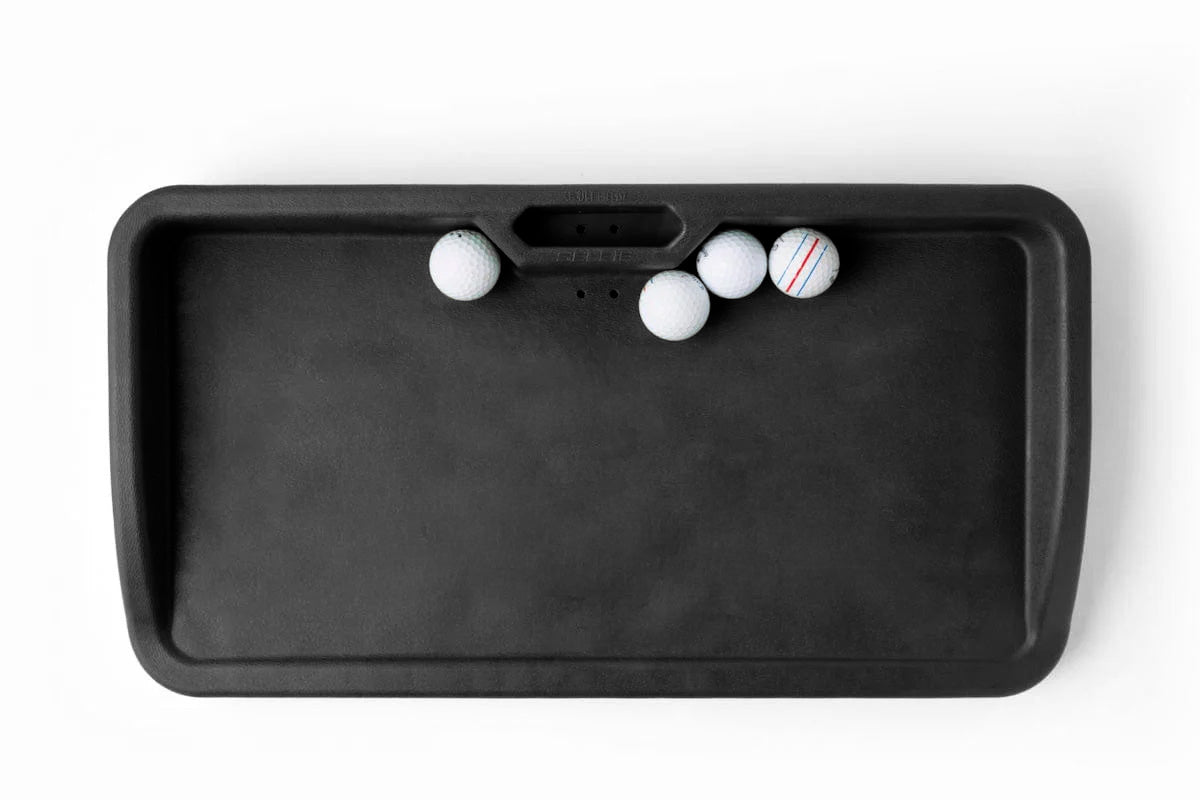 Top-down view of the official SKYTRAK durable black molded polymer golf ball tray containing four white golf balls, including a striped alignment training ball, isolated on a clean white background for home simulator studio setups.