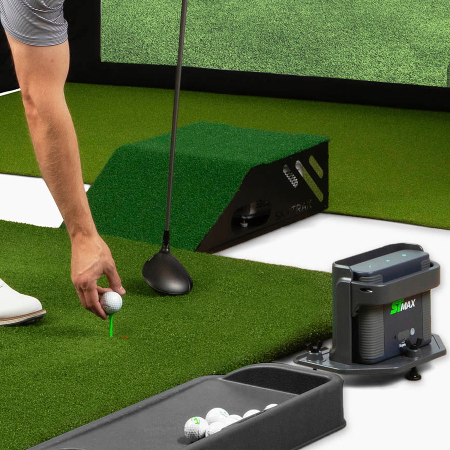 Golf simulator setup with a person preparing to hit a golf ball on a green surface.