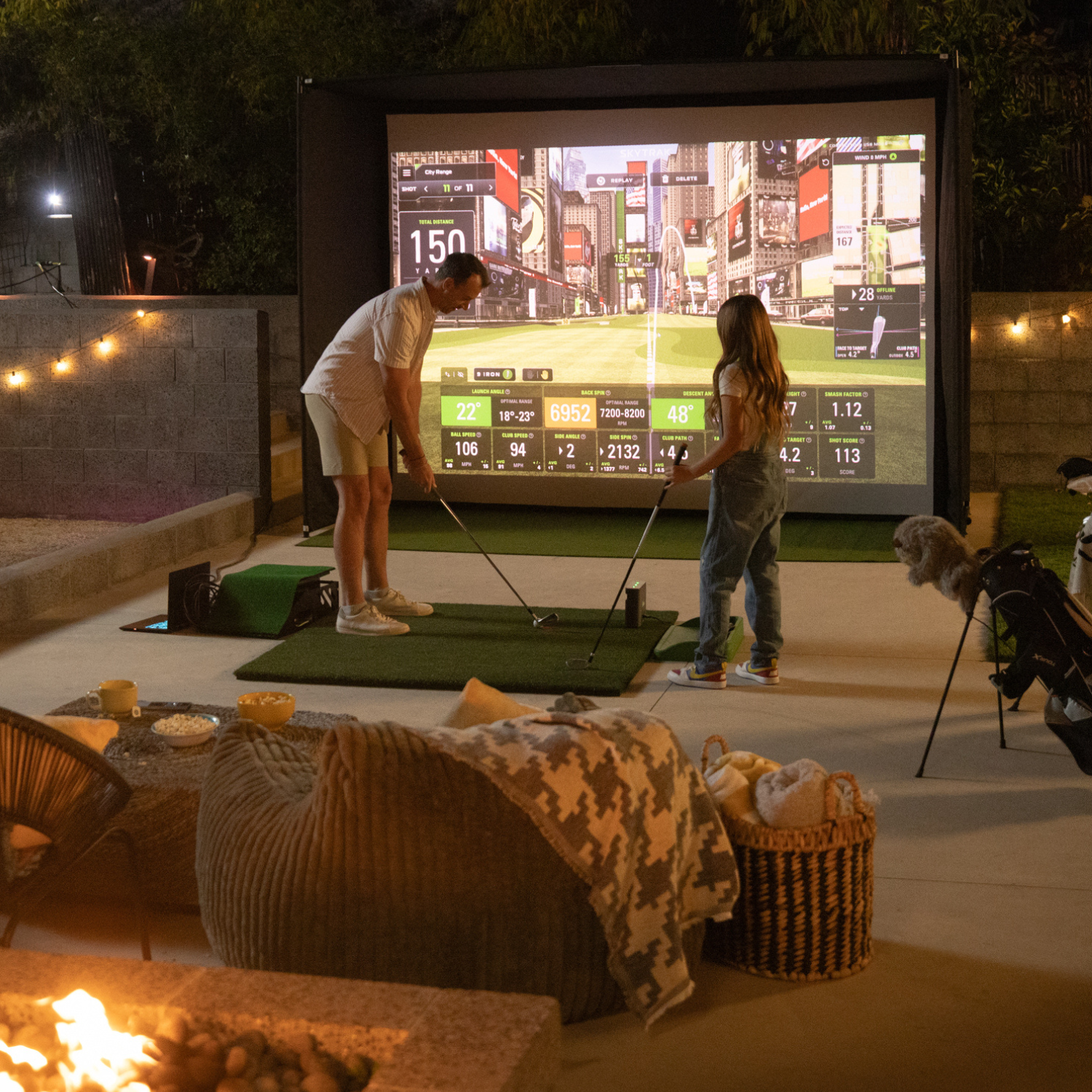 Two people playing a golf simulation game outdoors on a screen with a cozy outdoor setting.