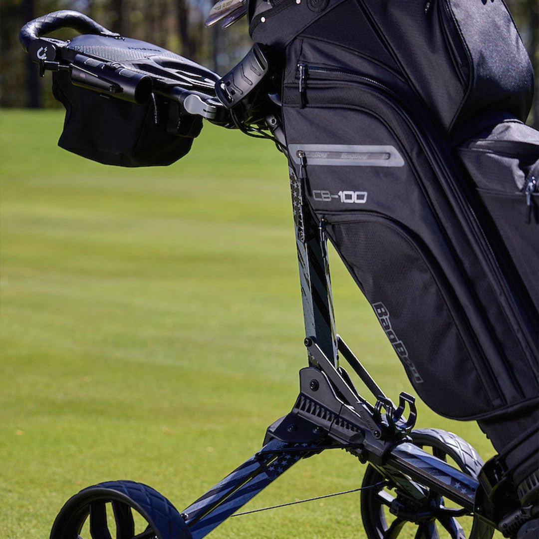Close-up detail of the Bag Boy CB-100 golf bag mounted on a push cart, showcasing the premium black fabric, zippered storage compartments, and durable design.