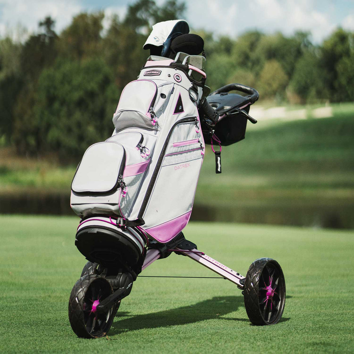 Lifestyle shot featuring the Bag Boy Nitron golf push cart paired with the Datrek DG-III golf bag, showcased in a vibrant pink and white colorway on a lush, professional golf course fairway.